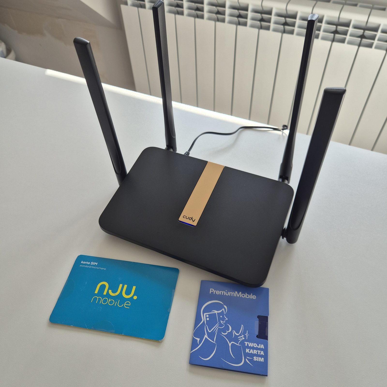 Router Cudy z czterema antenami na białym biurku TELFOX w Siemiatyczach, obok karty SIM nju mobile i Premium Mobile — internet mobilny do domu bez umowy na czas