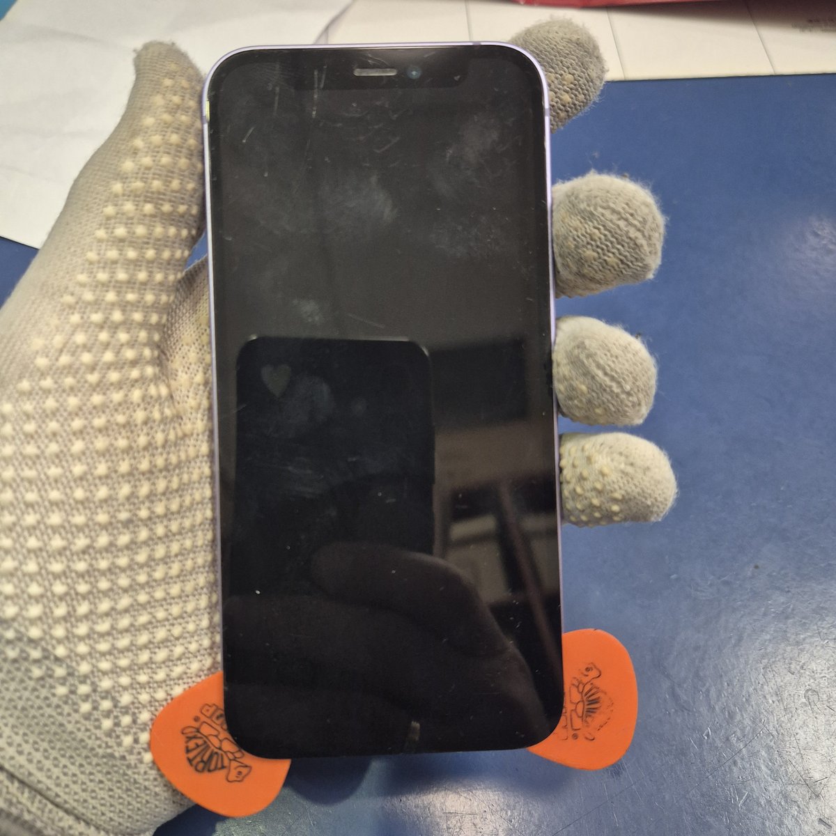 iPhone 12 mini z kostkami serwisowymi pod krawędzią ekranu — otwieranie telefonu przed wymianą baterii